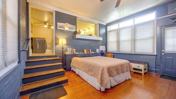 A bedroom with a bed, a nightstand, a dresser, a window with blinds, a ceiling fan, and a staircase.
