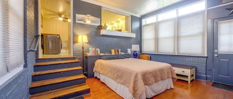 A bedroom with a bed, a nightstand, a dresser, a window with blinds, a ceiling fan, and a staircase.