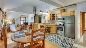 A modern kitchen with wooden cabinets, stainless steel appliances, and a dining area with a round table and chairs. - Deck & Wooded Views! 2 Mi to Frederick Gunn School (Washington)