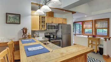 A kitchen with wooden cabinets, a stainless steel refrigerator, a microwave, and a stove. There is a dining table with blue placemats and wooden chairs.