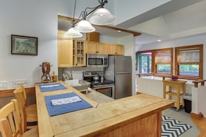 A kitchen with wooden cabinets, a stainless steel refrigerator, a microwave, and a stove. There is a dining table with blue placemats and wooden chairs. - Deck & Wooded Views! 2 Mi to Frederick Gunn School (Washington)