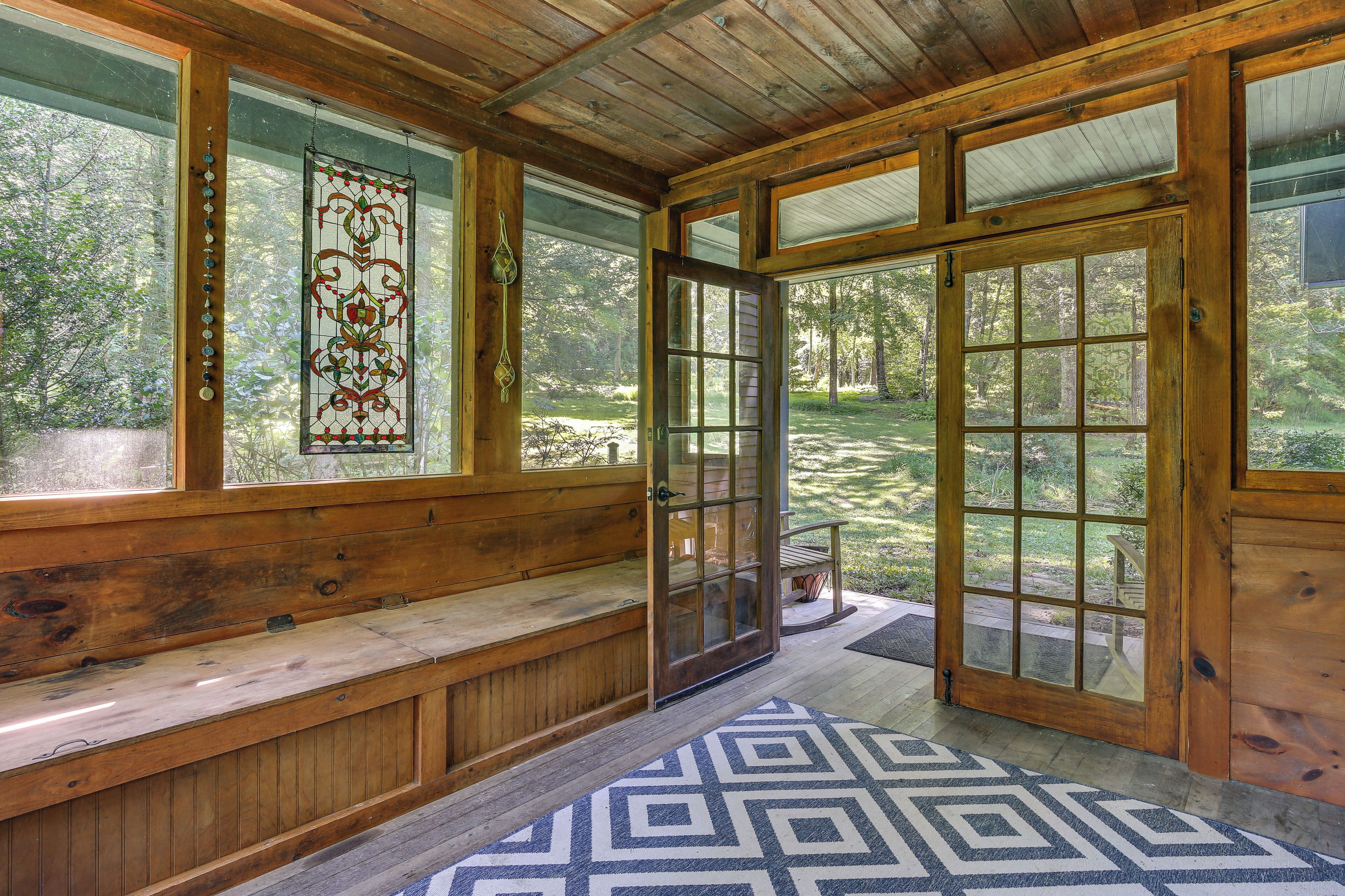 A wooden interior with a bench, a stained glass window, and a door leading to an outdoor area.