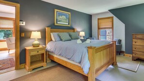 Een slaapkamer met een houten bed, twee nachtkastjes met lampen, een ingelijst schilderij aan de muur en uitzicht door een raam met jaloezieën.