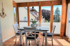 A dining area with a table and chairs, large windows, and a view of a residential neighborhood. - Holiday apartment House Mecklenburg 322202 (Kühlungsborn)
