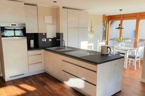 A modern kitchen with a central island, built-in oven, and a dining area with a table and chairs. - Holiday apartment House Mecklenburg 322202 (Kühlungsborn)