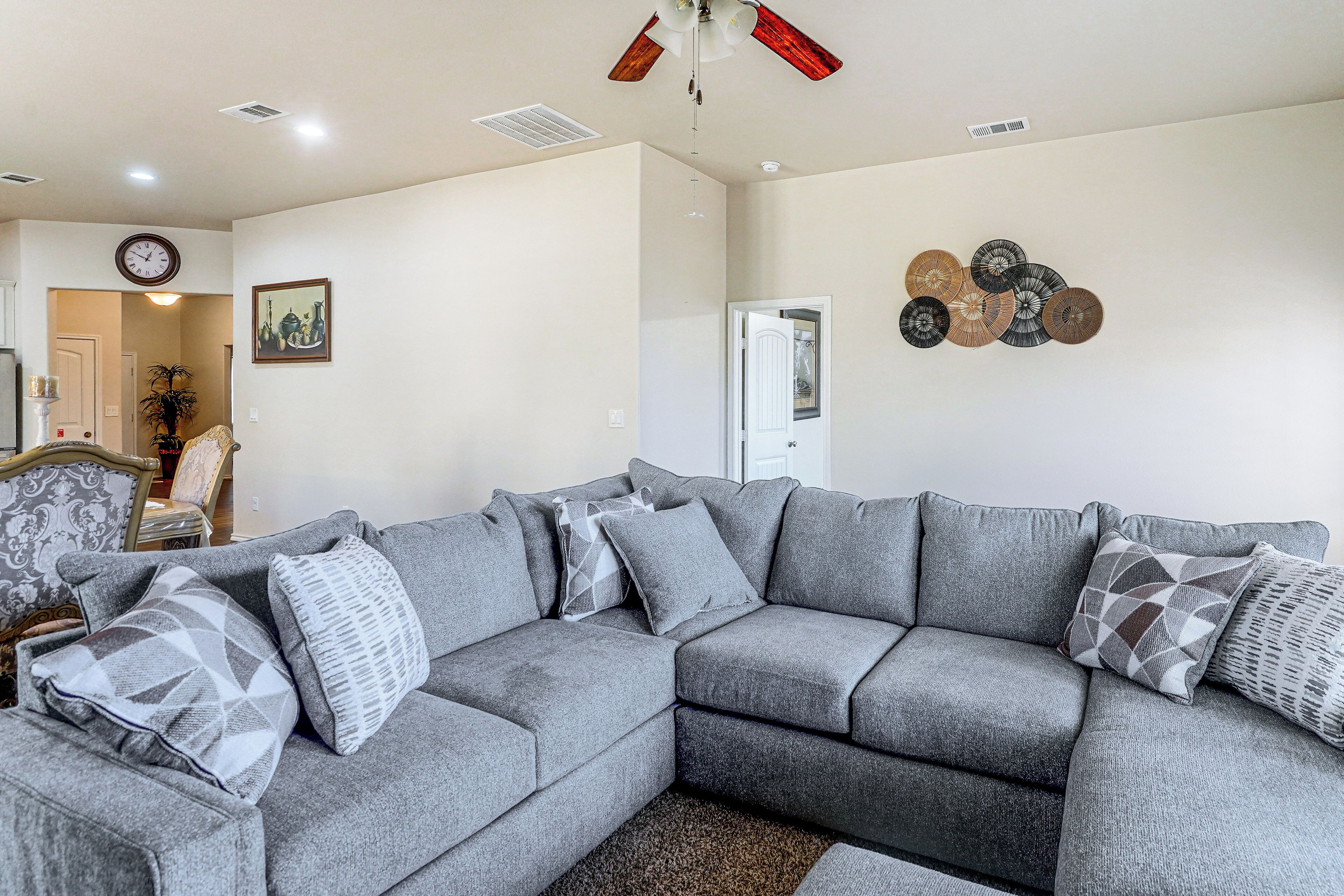 A living room with a sectional sofa, a clock, and a decorative wall piece.