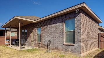 A two-story brick house with a covered patio and a visible outdoor grill.