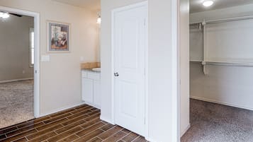A hallway with a white door, a bathroom with a shower, and a carpeted floor.