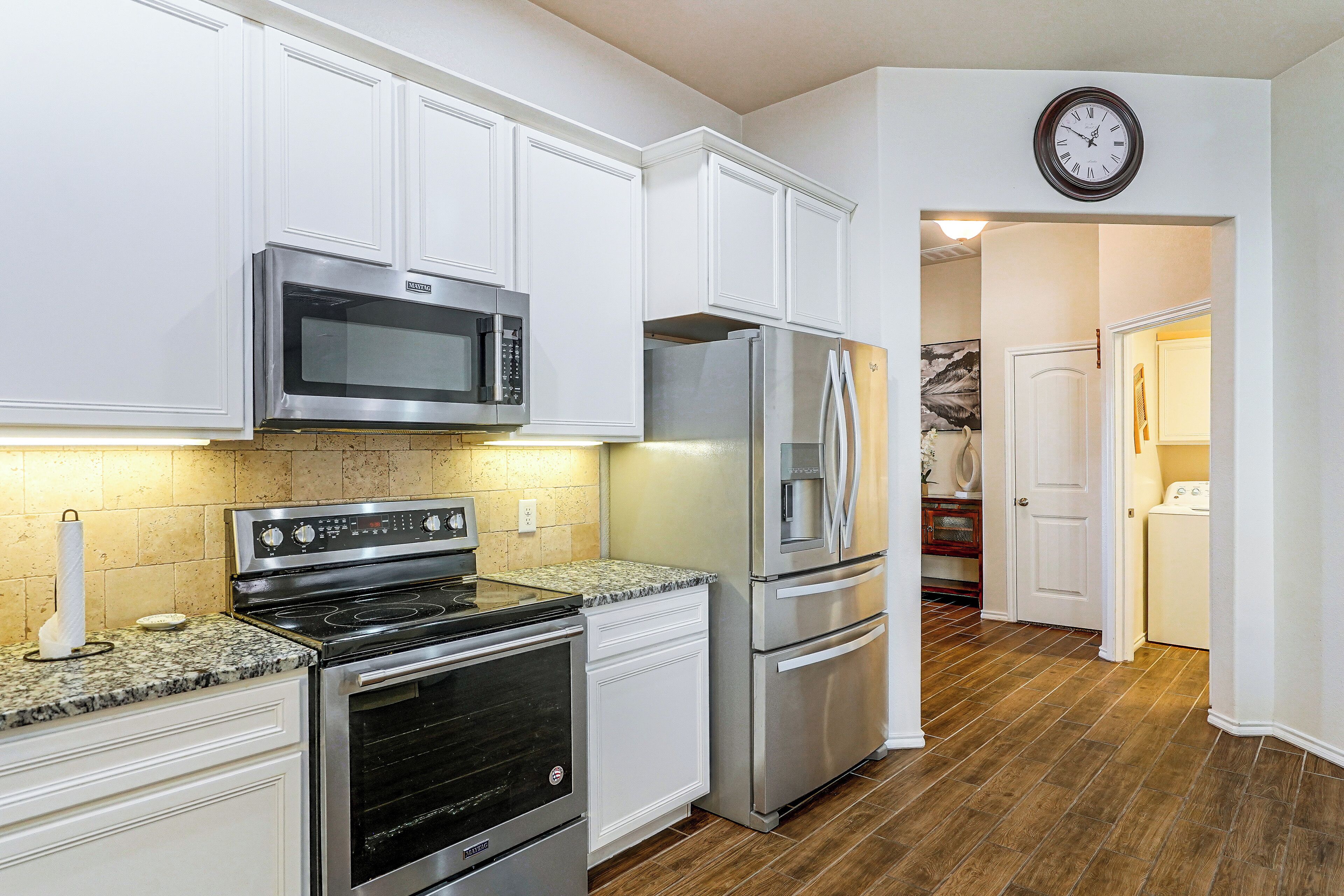 A modern kitchen with stainless steel appliances, white cabinetry, and a wooden floor.