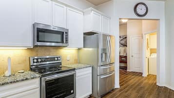 A modern kitchen with stainless steel appliances, white cabinetry, and a wooden floor.