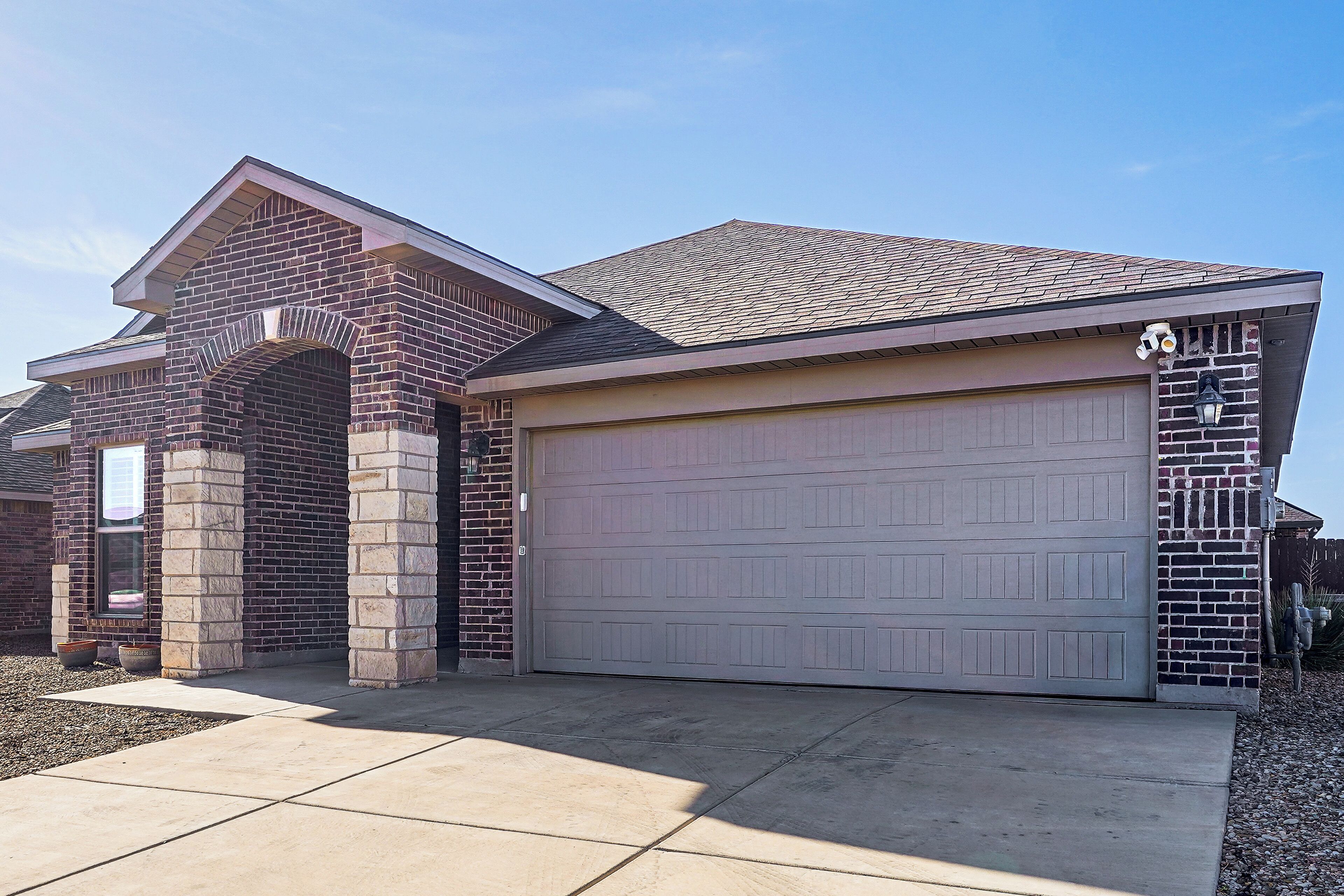 A residential building with a brick facade, a garage door, and a tiled driveway.