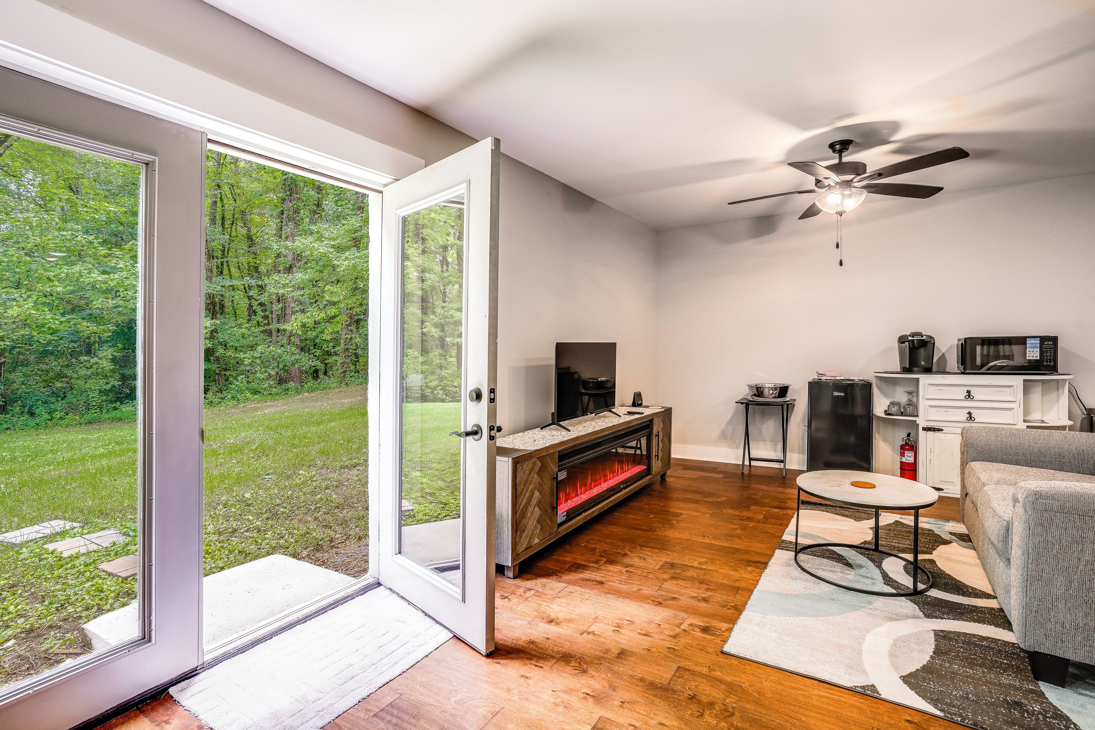 A room with a sliding glass door leading to a grassy yard, a fireplace, a ceiling fan, a small table, and a sofa.
