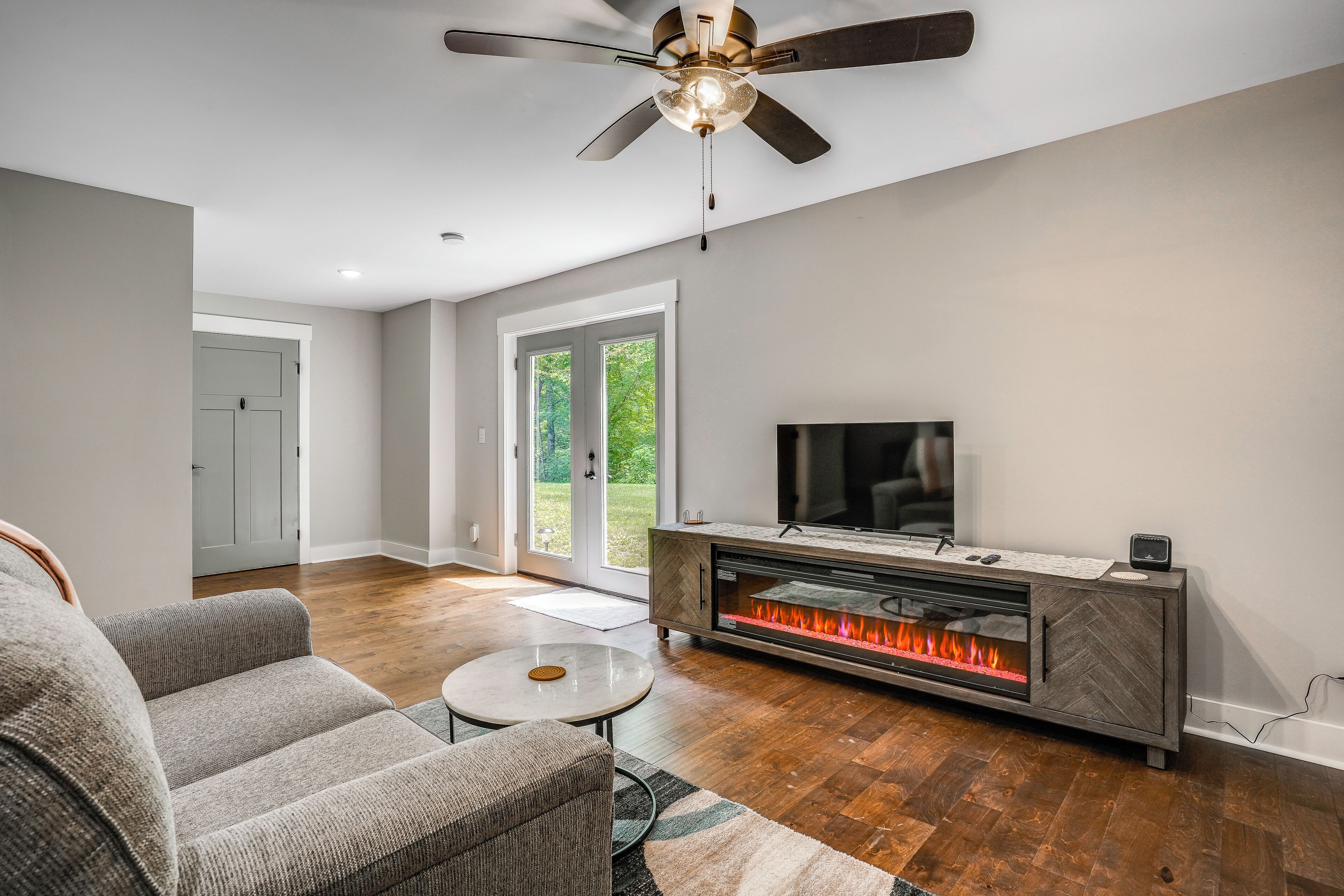 A modern living room with a fireplace, a ceiling fan, and a television.