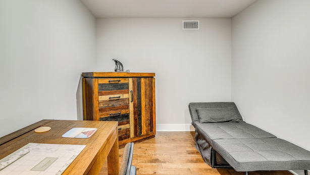 A small room with a wooden cabinet, a table with papers, a bench, and a white wall.