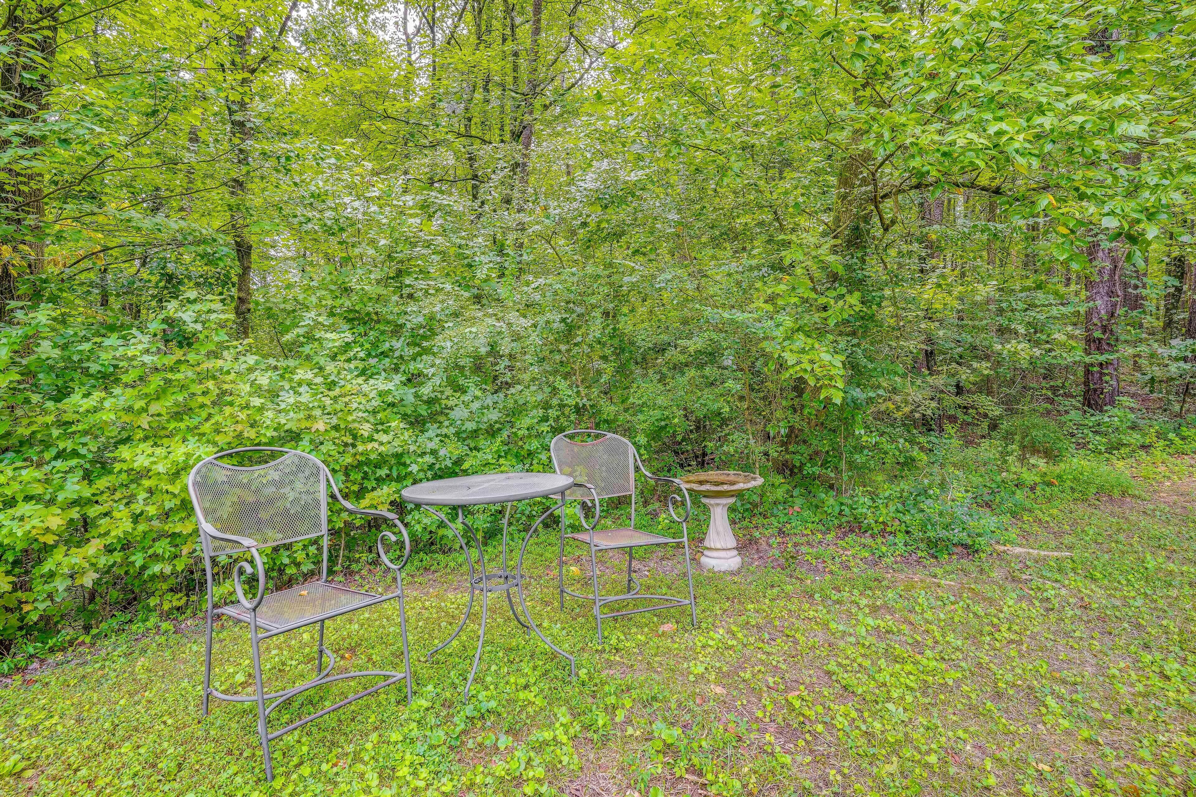 An outdoor seating area with metal chairs and a table, surrounded by dense green foliage.