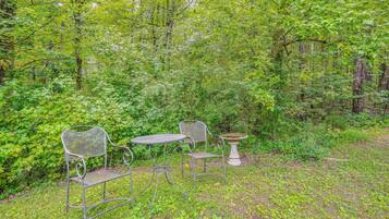 An outdoor seating area with metal chairs and a table, surrounded by dense green foliage.