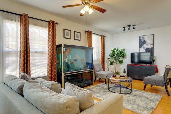 A living room with a sofa, a television, a fish tank, and a ceiling fan.