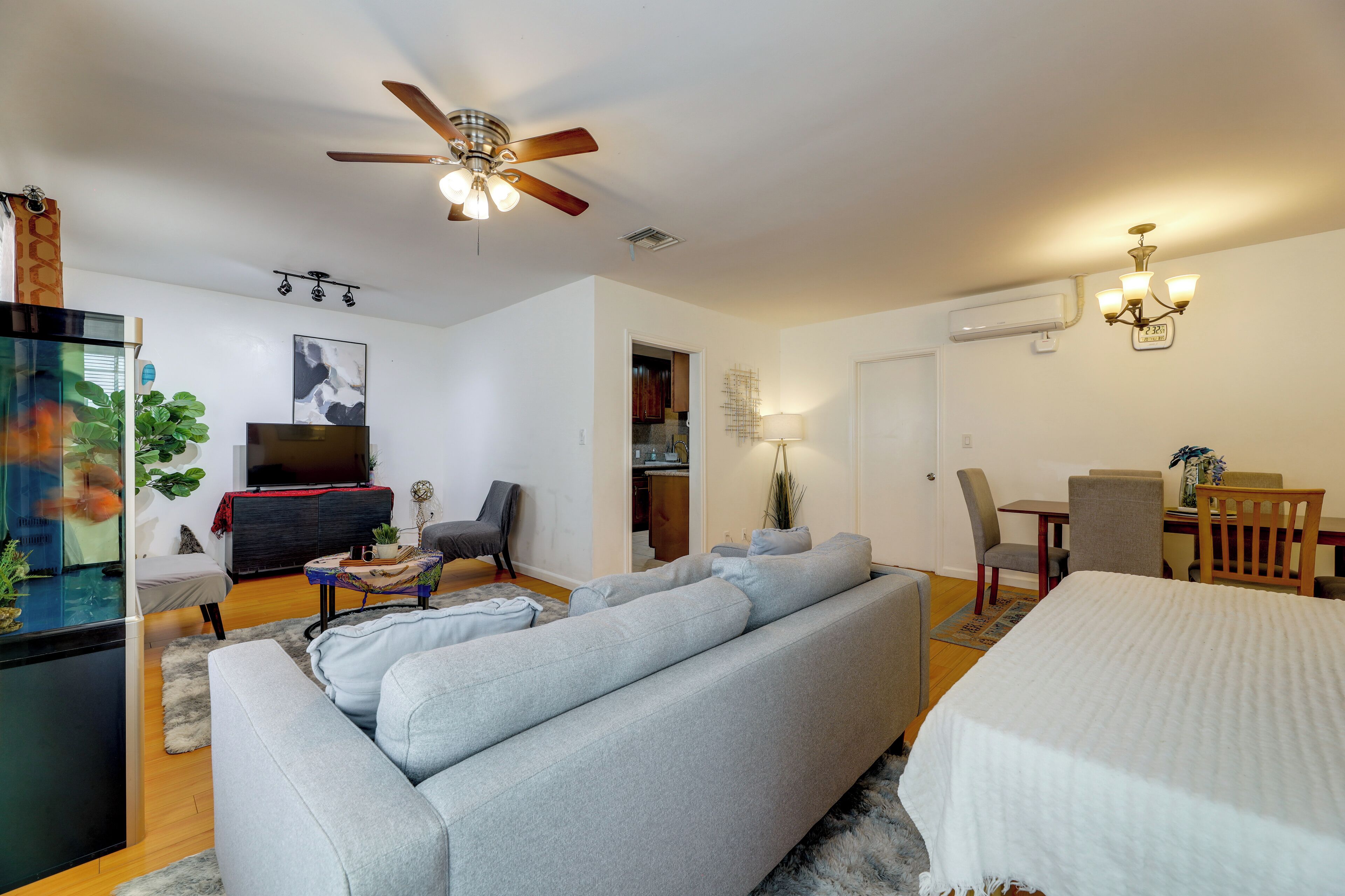 Ein modernes Wohnzimmer mit einem grauen Sofa, einem Fernseher, einem Deckenventilator und einem Essbereich mit Stühlen und einem Tisch.