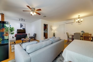 A modern living room with a grey sofa, a TV, a ceiling fan, and a dining area with chairs and a table.