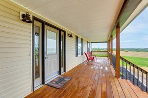 A wooden porch with a red chair, a welcome mat, and a view of the countryside.