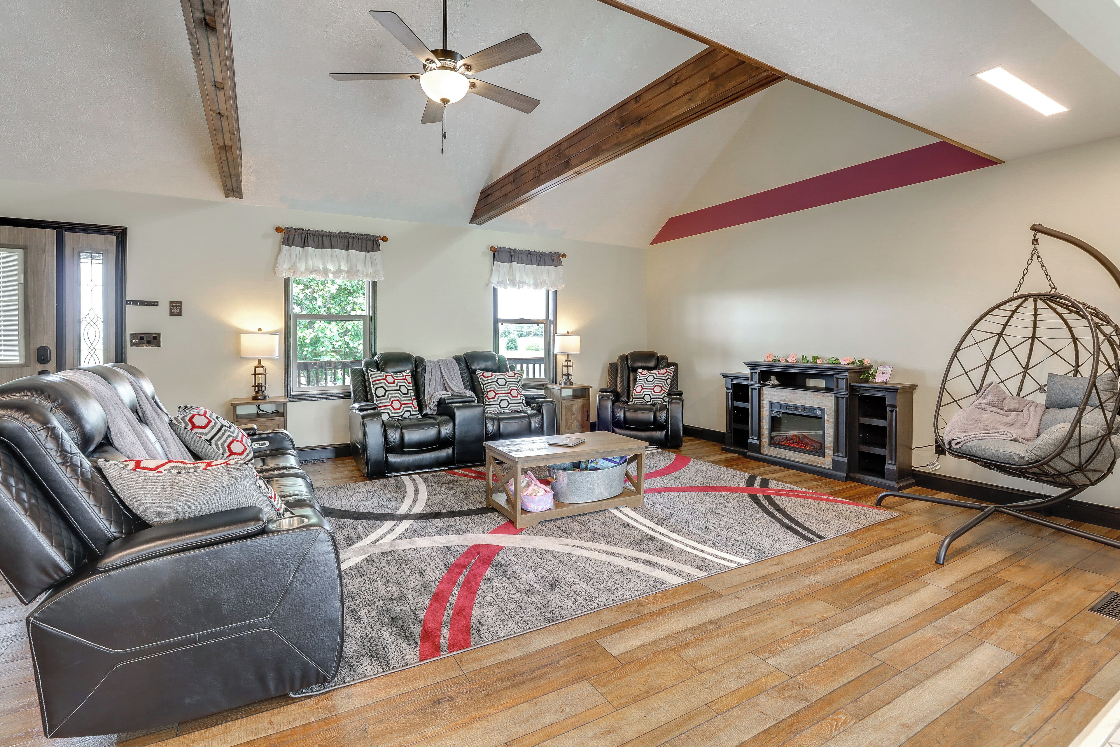 A spacious living room with a fireplace, leather sofas, a hanging chair, and a ceiling fan.