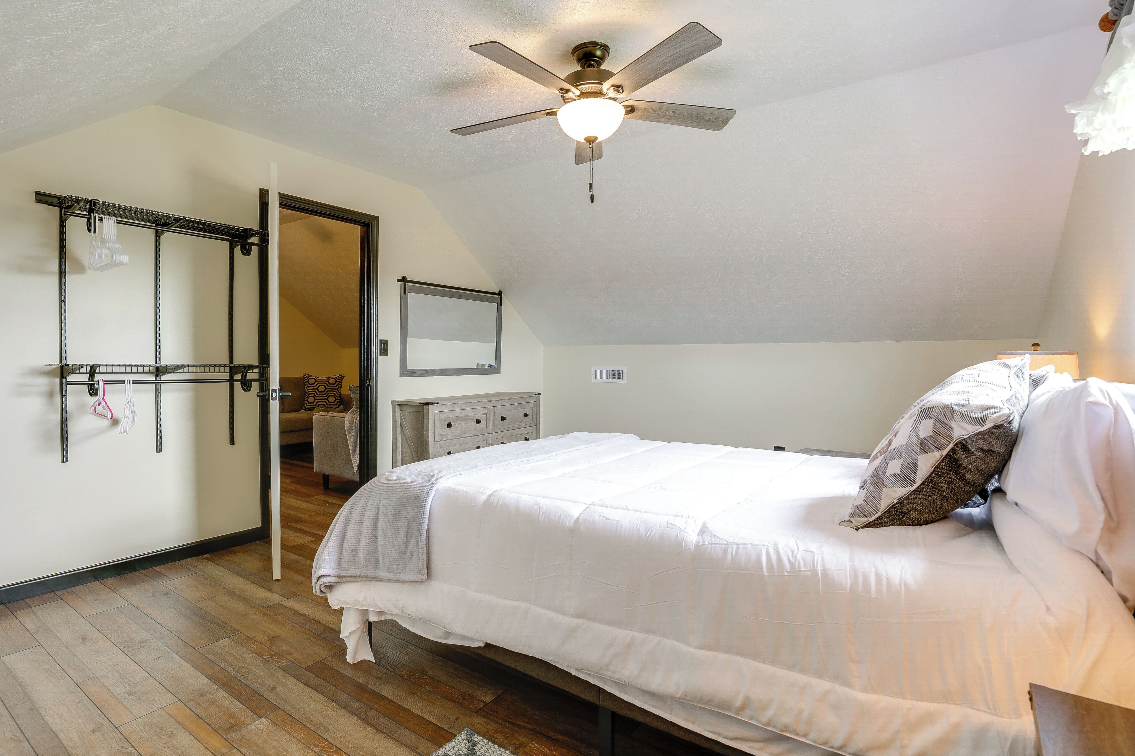 A bedroom with a bed, a ceiling fan, a dresser, and a mirror.