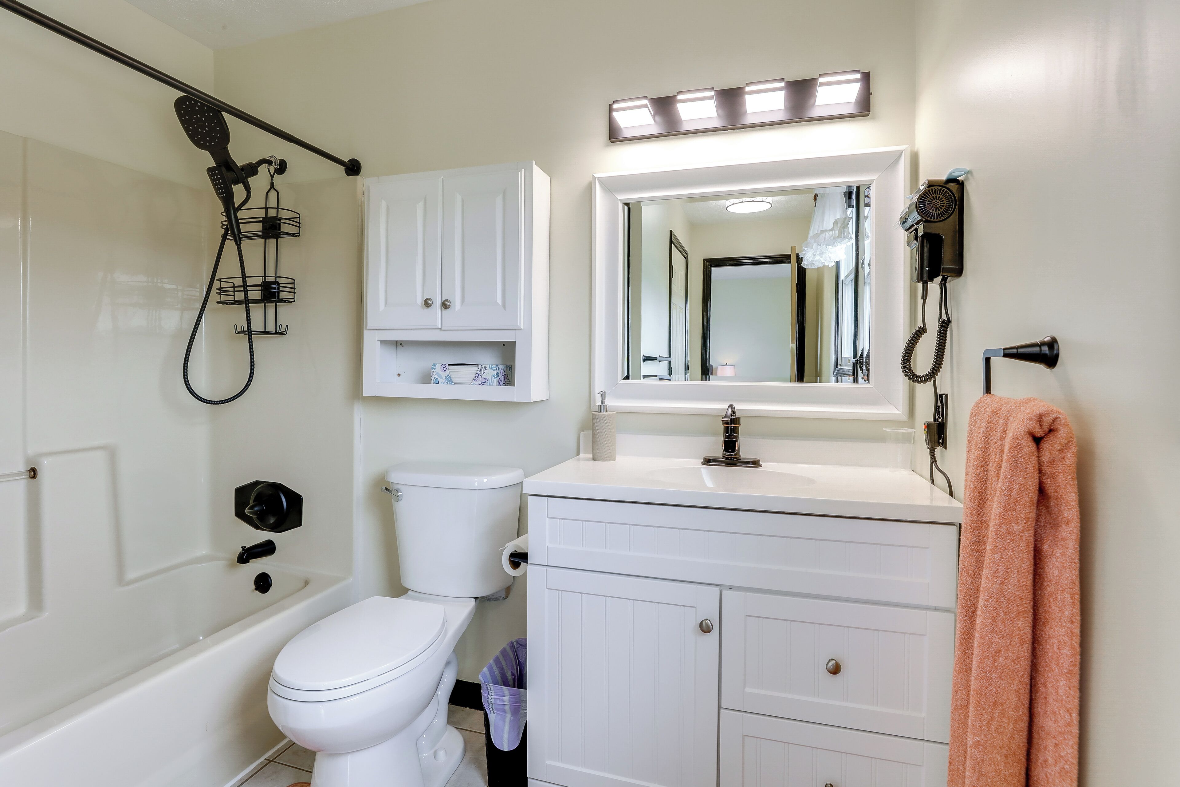 A bathroom with a white toilet, a vanity with a mirror, a hairdryer, and a towel rack.