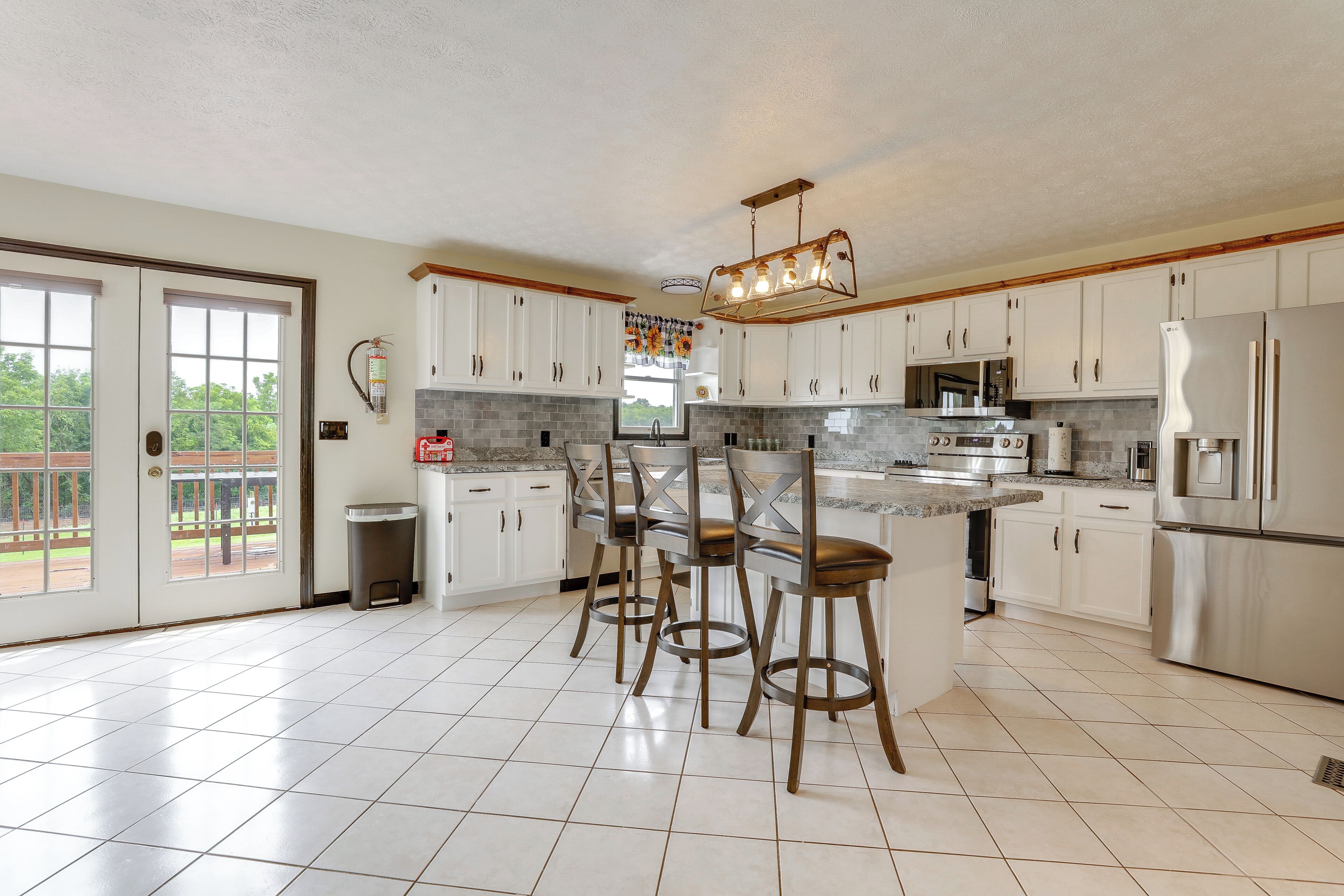 A kitchen with white cabinets, a stainless steel refrigerator, an island with bar stools, and a fire extinguisher on the wall.