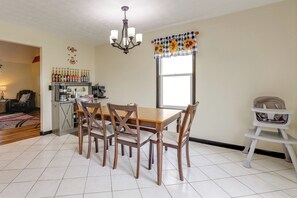 A dining area with a wooden table and chairs, a chandelier, a kitchen area with coffee-making equipment, and a window with a sunflower curtain. - Game Room & Countryside Views! Salvisa Family Gem (Salvisa)