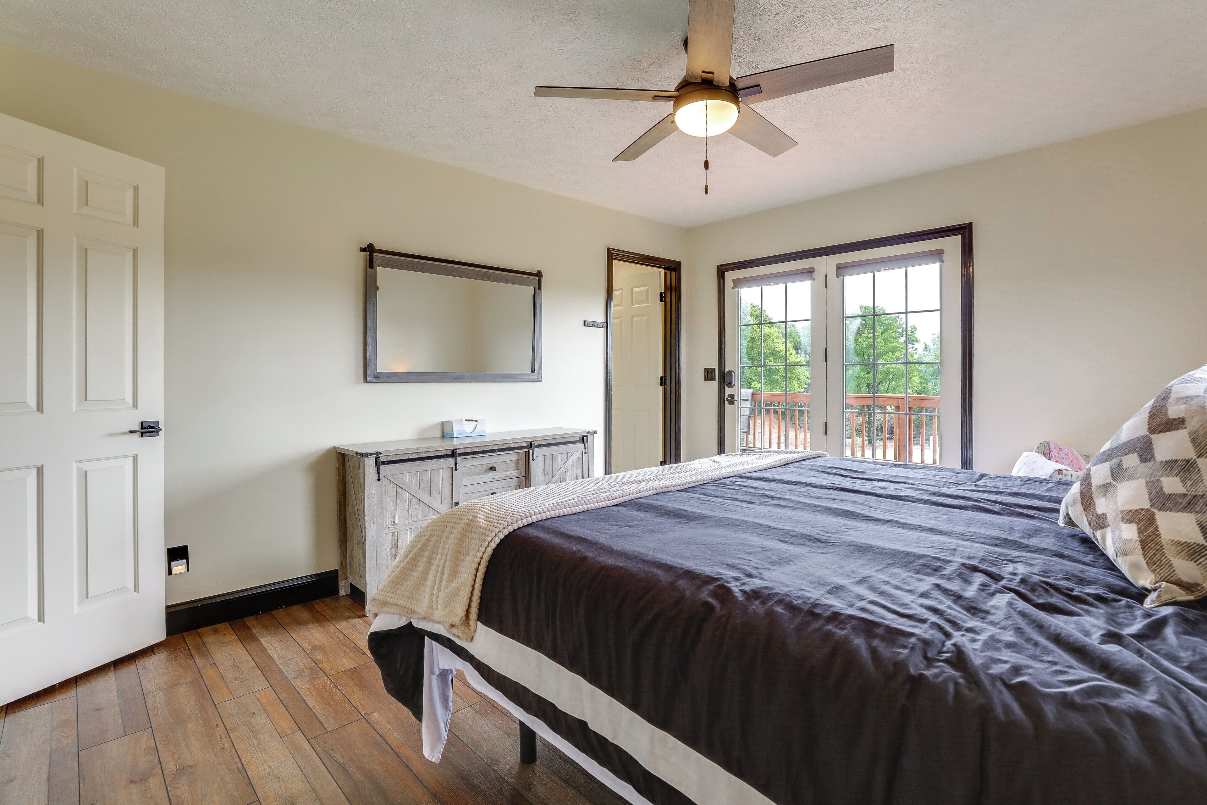 A bedroom with a bed, a ceiling fan, a dresser, a mirror, and a door leading to a balcony.