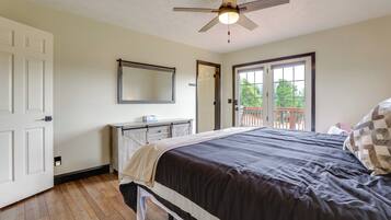 A bedroom with a bed, a ceiling fan, a dresser, a mirror, and a door leading to a balcony.