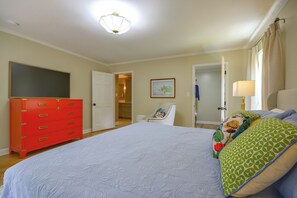 A bedroom with a large bed, a red dresser, a door leading to a bathroom, and a painting on the wall.