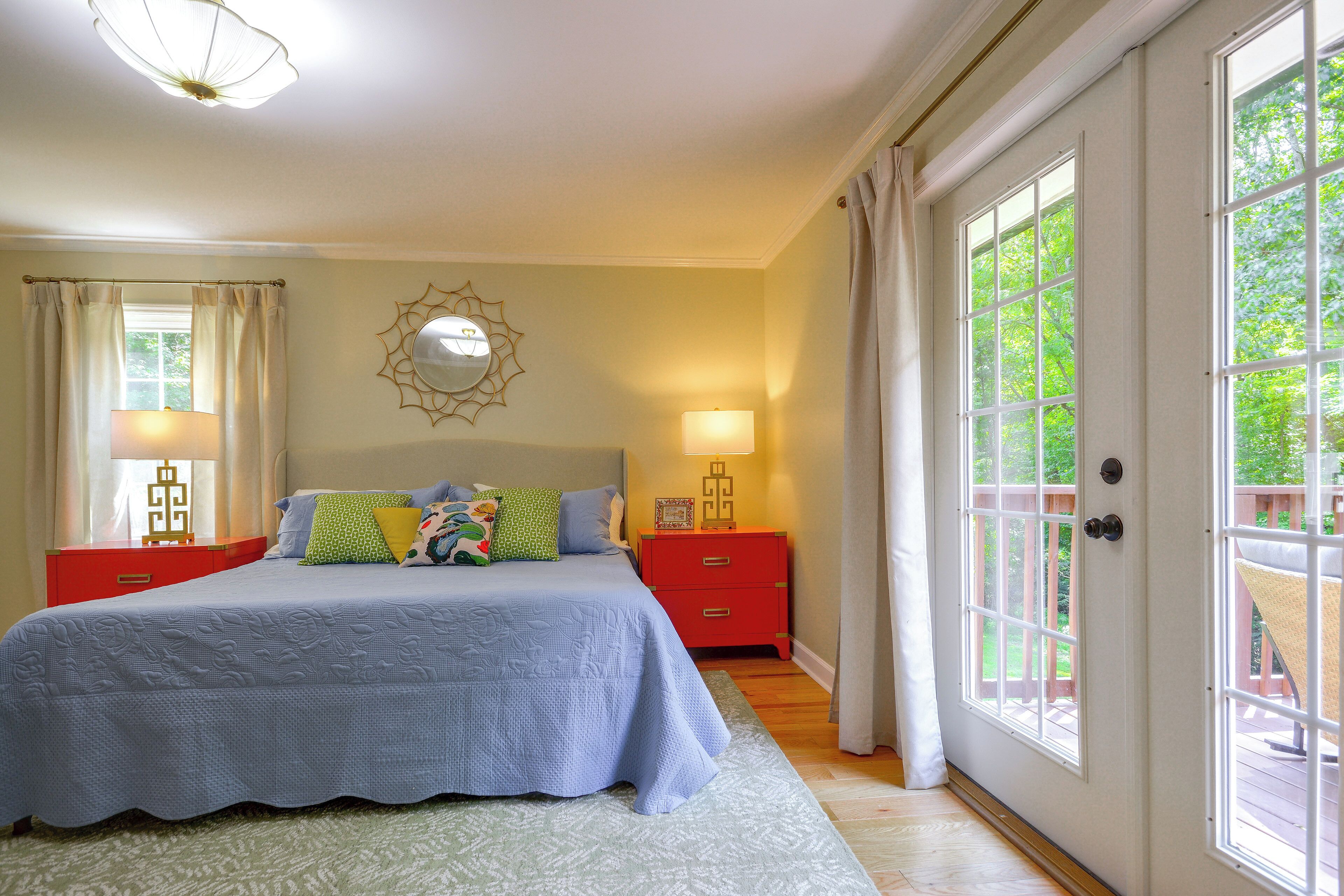 A bedroom with a bed, nightstands, a mirror, and a view through a door.