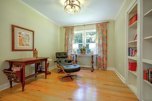 A room with hardwood flooring, a black leather chair, a wooden table with a bottle, a framed picture, a window with curtains, and a bookshelf. - Office, Deck, Yard: Thomasville Gem on Golf Course (Thomasville)