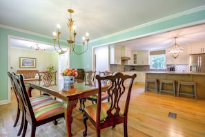 A dining area with a wooden table and chairs, a chandelier, and a view into the kitchen.