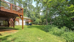 A wooden deck with a staircase leading to a covered area, surrounded by a well-maintained lawn and dense trees. - Office, Deck, Yard: Thomasville Gem on Golf Course (Thomasville)