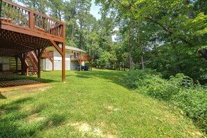 A wooden deck with a staircase leading to a covered area, surrounded by a well-maintained lawn and dense trees. - Office, Deck, Yard: Thomasville Gem on Golf Course (Thomasville)
