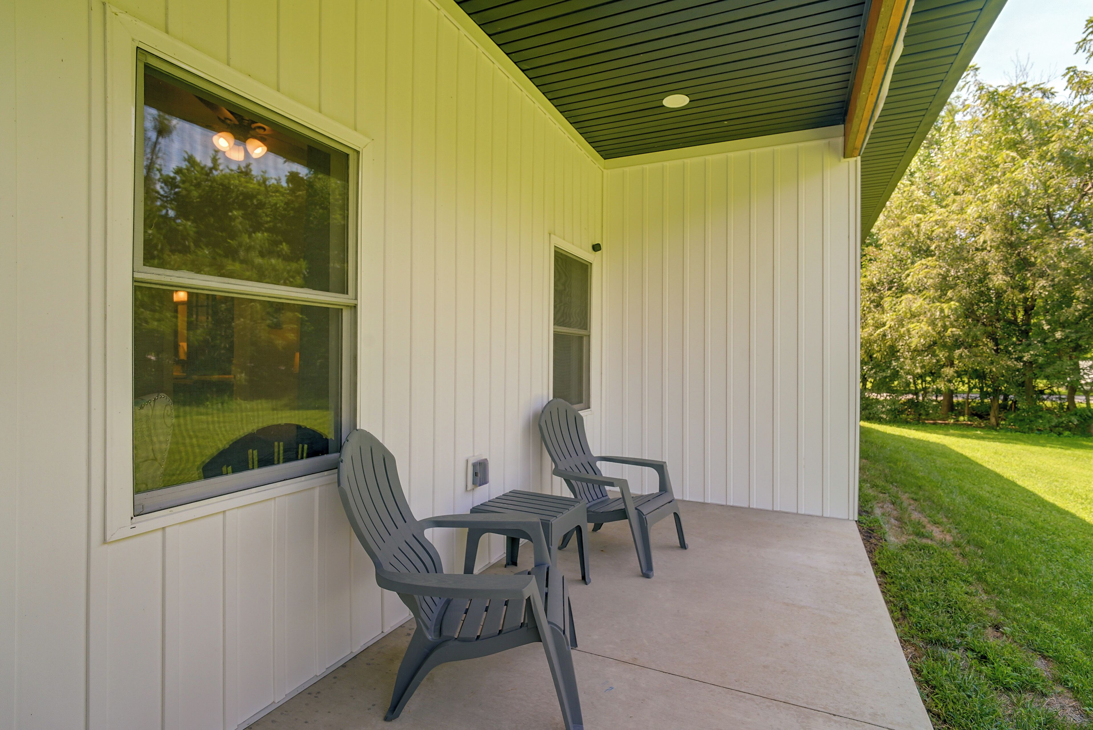 A covered porch with two chairs and a table, white siding walls, and a view of a green lawn.