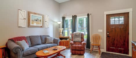 Un salon avec un canapé, un fauteuil, une table basse et une porte.