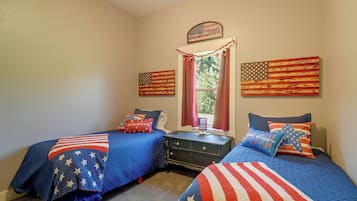 A bedroom with two beds, each covered with a blue quilt featuring white stars, and a window with red curtains.