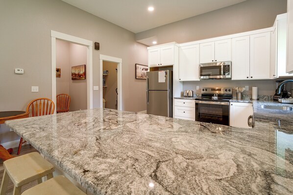 A kitchen with white cabinets, a stainless steel refrigerator, a microwave, and a granite countertop.