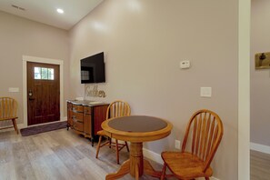 A dining area with a round table and four chairs, a wooden cabinet, a flat-screen TV mounted on the wall, and a door with a window.