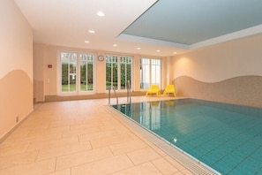 An indoor swimming pool with clear glass walls, yellow chairs, and a tiled floor. - Holiday apartment Dünenschloss 319668 (Kühlungsborn)