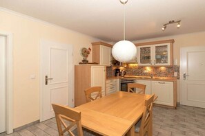 A kitchen with a wooden dining table, chairs, cabinets, and a hanging light fixture. - Holiday apartment Dünenschloss 319668 (Kühlungsborn)