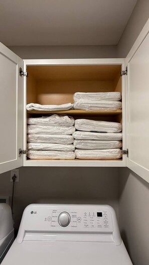 A white washing machine with a control panel and a cabinet above it containing folded white towels. - Luxury Ranch w/ Vaulted Ceilings & Chef's Kitchen (Charlotte)