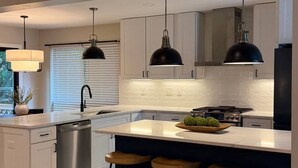 A modern kitchen with a central island, bar stools, pendant lighting, and a dishwasher.