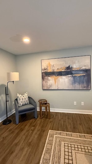 A room with a large abstract painting on the wall, a floor lamp, a sofa with a patterned cushion, and a small wooden stool. - Luxury Ranch w/ Vaulted Ceilings & Chef's Kitchen (Charlotte)
