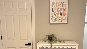 A room with a white door, a white console table with shelves, and a framed motivational quote on the wall.