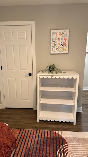 A room with a white door, a white console table with shelves, and a framed motivational quote on the wall.