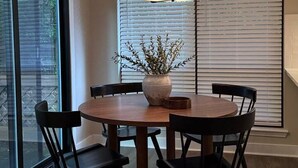 A dining area with a round table, four chairs, a vase with branches, and a hanging light fixture.